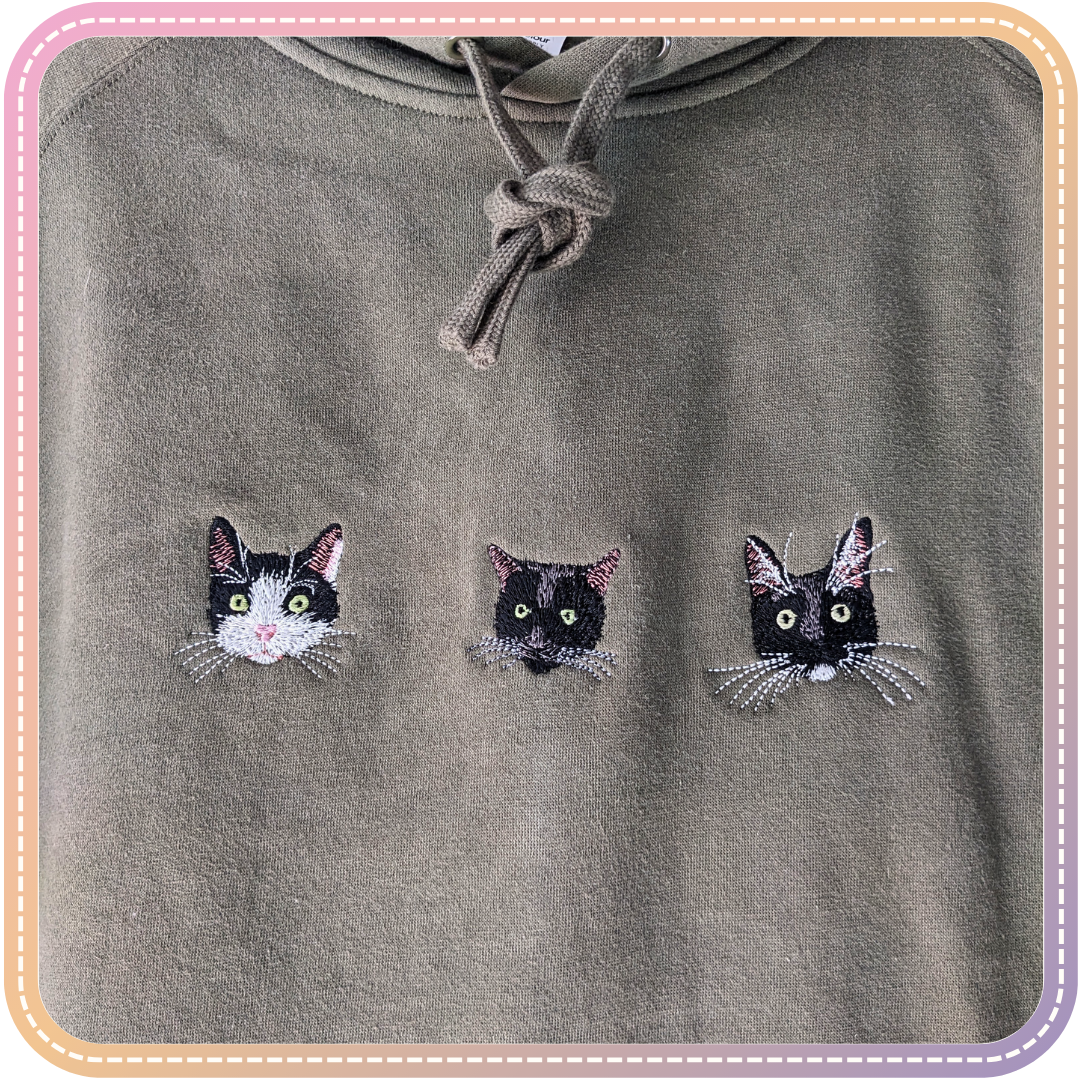 close up of a green hoodie with three cats embroidered