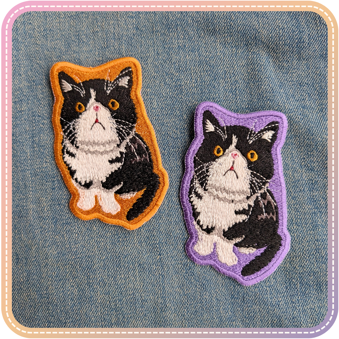 Two embroidery patches of Maude, a flat faced black and white tuxedo cat. One with a purple background and the other with an orange background