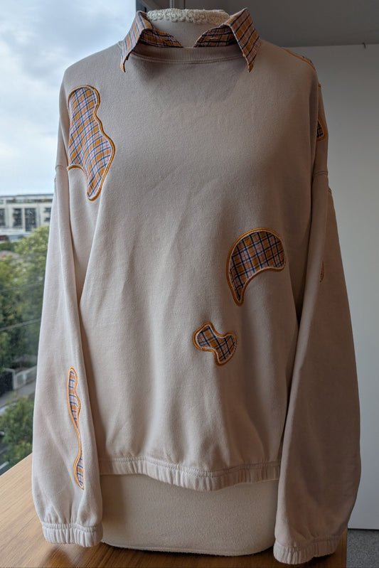beige crew neck upcycled with embroidery blob cut outs over a blue and orange checkered shirt.
