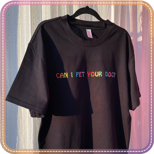 Black t-shirt with colorful text 'CAN I PET YOUR DOG?' on a hanger